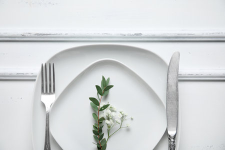 Plates with silver cutlery and flowers on white wooden backgroundの写真素材