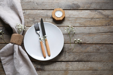 Plate with folded napkin, cutlery and candle on brown wooden background