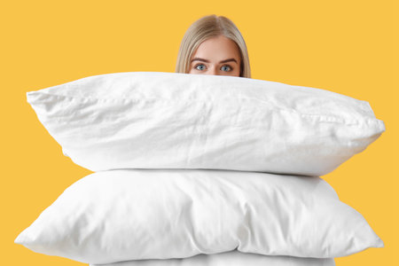 Young woman with pillows on yellow backgroundの写真素材