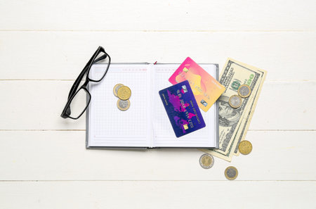Open notebook with credit cards, money and eyeglasses on white wooden table