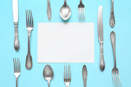 Frame made of blank card and stainless steel cutlery on blue backgroundの写真素材