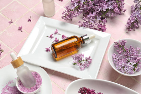 Bottles of lilac essential oil, sea salt and flowers on pink background, closeupの写真素材
