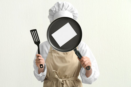 Female chef holding frying pan with blank card and spatula on light backgroundの写真素材