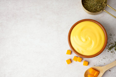 Bowl with tasty cheddar cheese sauce and measuring cup of rosemary on white grunge backgroundの写真素材