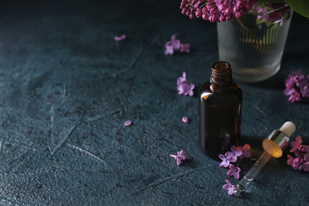 Bottle of cosmetic oil with beautiful lilac flowers on dark tableの写真素材