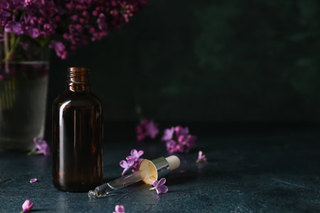 Bottle of cosmetic oil with beautiful lilac flowers on dark tableの写真素材