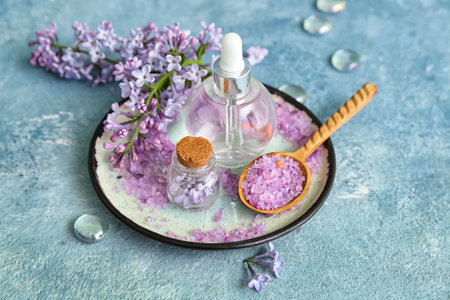 Bottles of cosmetic oil with beautiful lilac flowers and sea salt on blue tableの写真素材