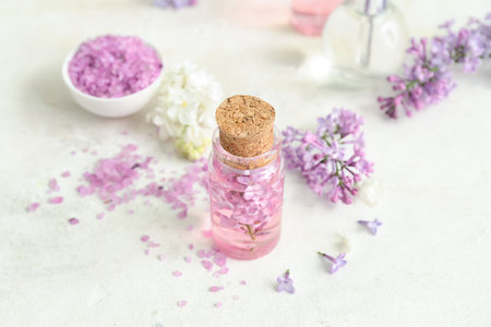 Bottles of cosmetic oil with beautiful lilac flowers and sea salt on white tableの写真素材