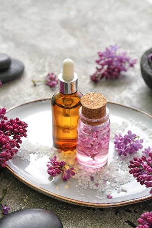 Bottles of cosmetic oil with beautiful lilac flowers and sea salt on gray tableの写真素材
