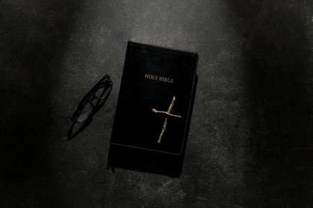 Holy Bible with wooden cross and eyeglasses on black backgroundの写真素材