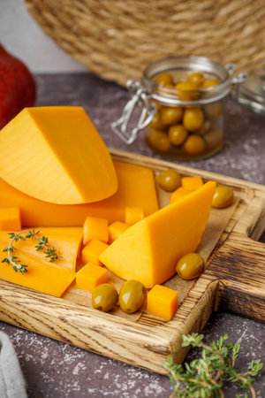 Board with tasty cheddar cheese, olives and thyme on grunge background, closeupの写真素材