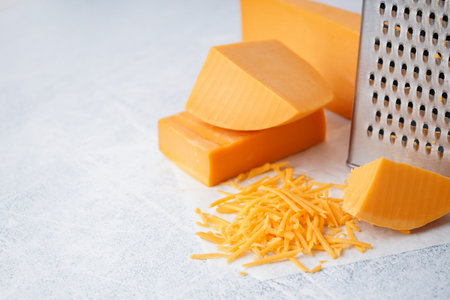 Tasty cheddar cheese and grater on light background, closeupの写真素材