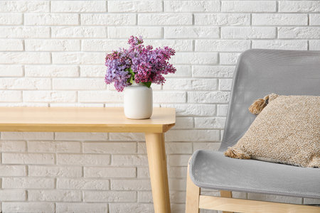Vase with beautiful lilac flowers on wooden table near light brick wallの写真素材