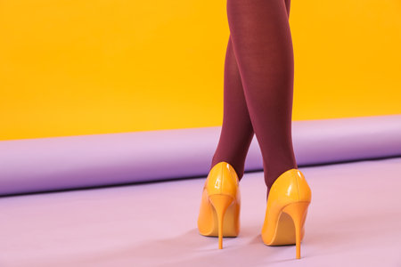 Female legs in black tights and yellow high heels on color background, back viewの写真素材