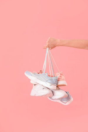 Female hand with many sneakers on pink backgroundの写真素材