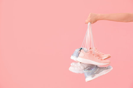 Female hand with many sneakers on pink backgroundの写真素材