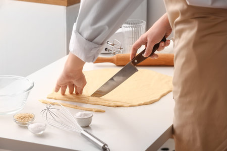 Woman cutting dough for Italian Grissini at white table in kitchen