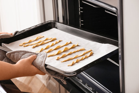 Woman putting baking tray with raw Italian Grissini into ovenの写真素材