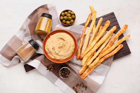 Bowl with tasty hummus and Italian Grissini on light background