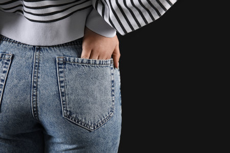 Young woman in stylish jeans on black background, back viewの写真素材