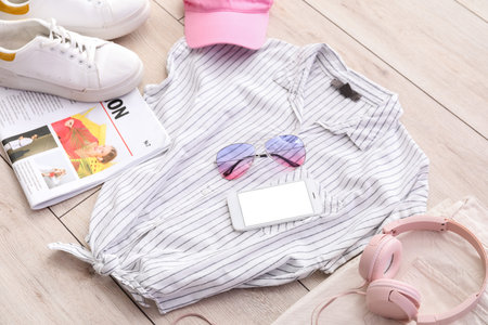 Stylish clothes with accessories, headphones, mobile phone and newspaper on light wooden floor