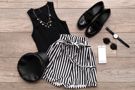 Stylish clothes with accessories, shoes and mobile phone on wooden floor