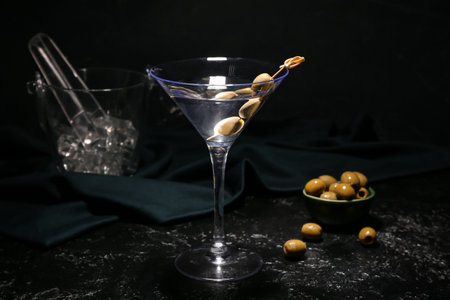 Glass of tasty martini with green olives and ice cubes on dark backgroundの写真素材