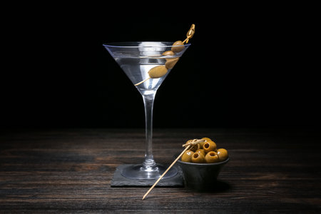 Glass of tasty martini and green olives on dark wooden tableの写真素材