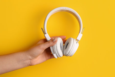Woman holding modern white headphones on yellow backgroundの写真素材