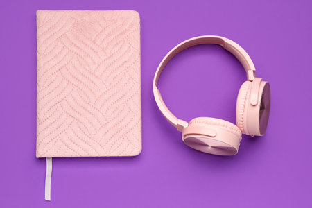 Notebook with modern pink headphones on purple backgroundの写真素材