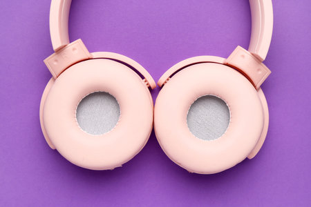 Modern pink headphones on purple background