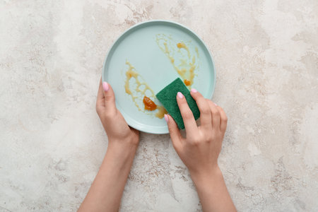 Female hands washing dirty plate with sponge on white grunge backgroundの写真素材