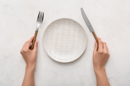 Female hands with cutlery and empty plate on white tableの写真素材