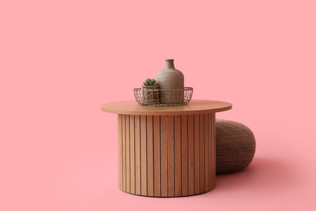 Wooden coffee table with jug, houseplant and pouf on pink backgroundの写真素材
