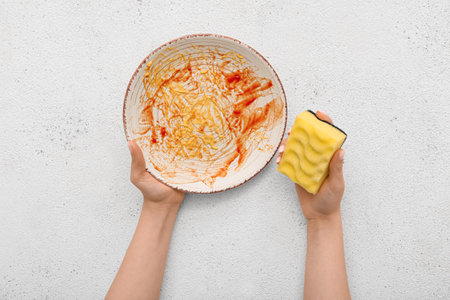 Female hands washing dirty plate with sponge on white grunge backgroundの写真素材