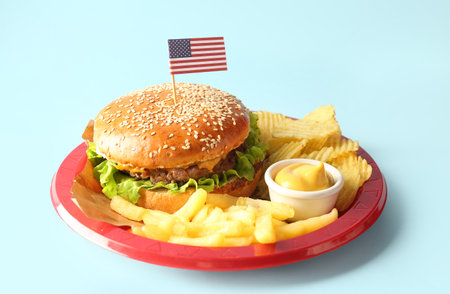 Plate with tasty burger, french fries, potato chips and sauce on color background. memorial day celebrationの写真素材