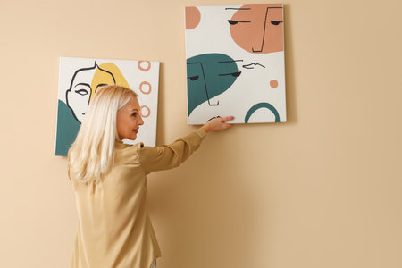 Mature woman hanging painting on beige wallの写真素材