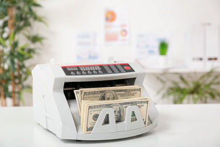 Modern cash counting machine with dollar banknotes on table in officeの写真素材