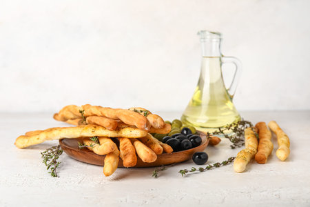 Plate with tasty Italian Grissini, thyme, olives and oil on light background