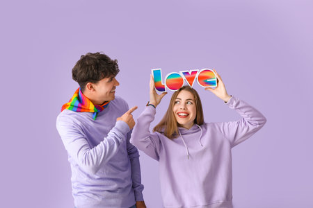 Young couple with word LOVE on lilac background. Pride Monthの写真素材