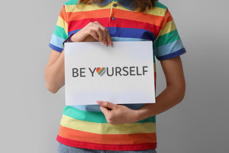 Young woman holding paper with text BE YOURSELF on light background, closeup. Pride Monthの写真素材