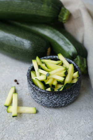 Fresh green zucchini and bowl with slices on gray backgroundの写真素材