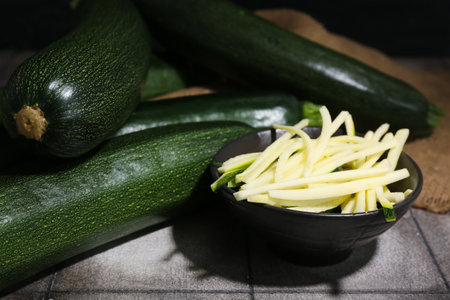 Many fresh zucchini and bowl with slices on gray tile tableの写真素材