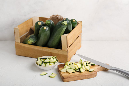 Wooden box with many fresh zucchini and bowl of slices on white backgroundの写真素材