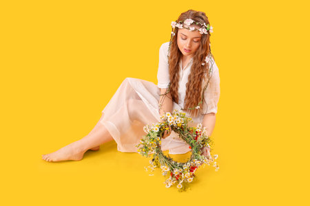 Beautiful young woman with flower wreath on yellow background. summer solsticeの写真素材