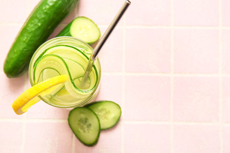 Glass of infused water with cucumber slices on pink tile tableの写真素材