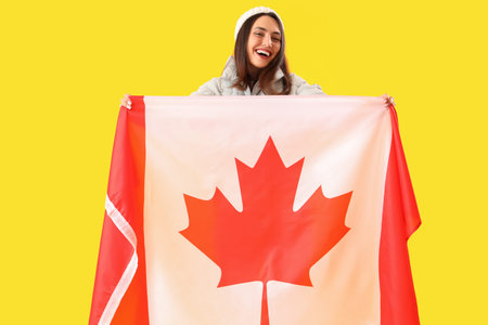 Young woman in warm hat with flag of Canada on yellow backgroundの写真素材