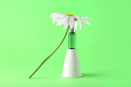 Bottle of essential oil on podium and chamomile flower on color backgroundの写真素材