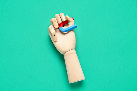 Wooden hand with horseshoe shaped mini magnet on green backgroundの写真素材