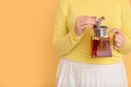 Beautiful young woman with teapot of chamomile tea near yellow wallの写真素材